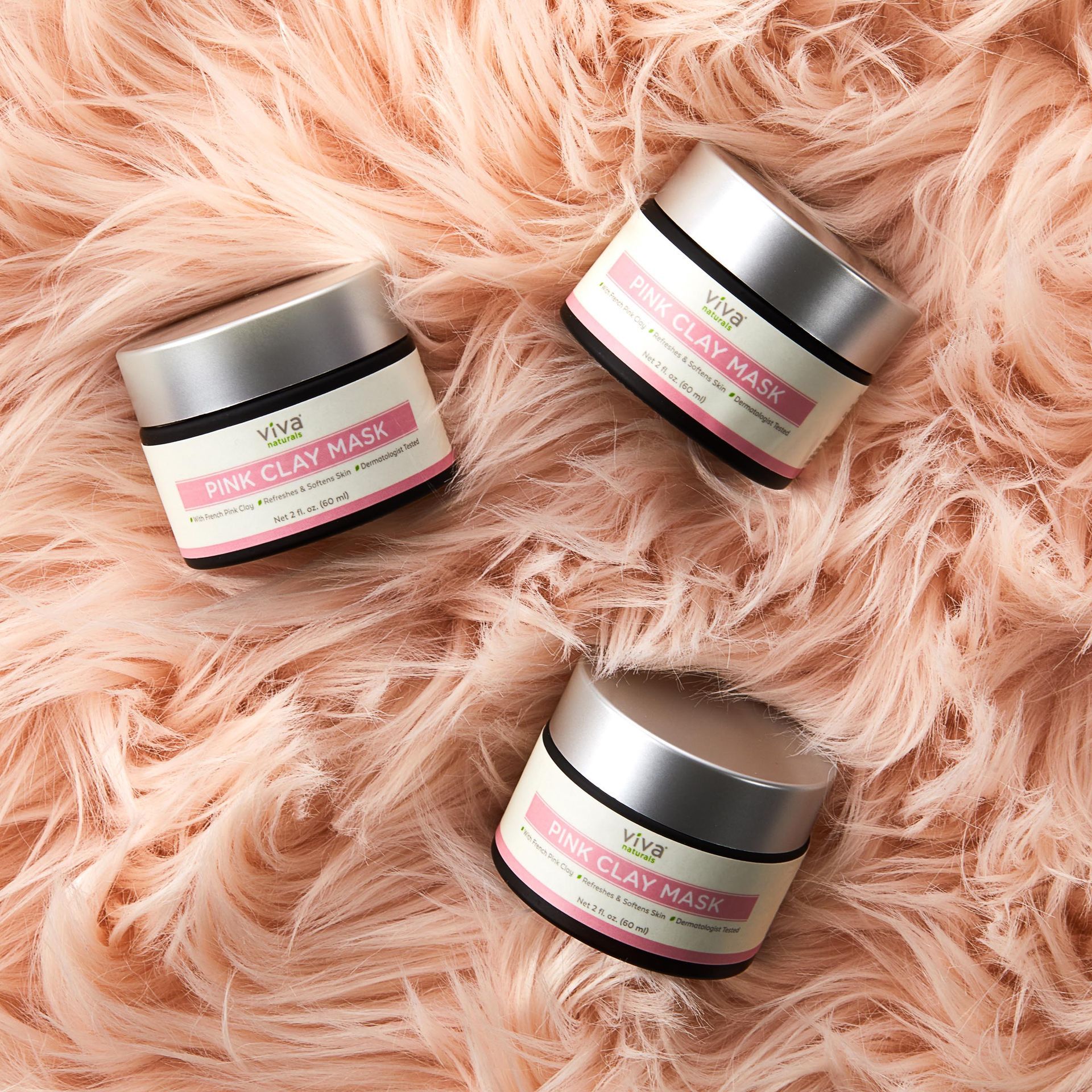 Three jars of pink clay mask are sitting on a pink furry surface.