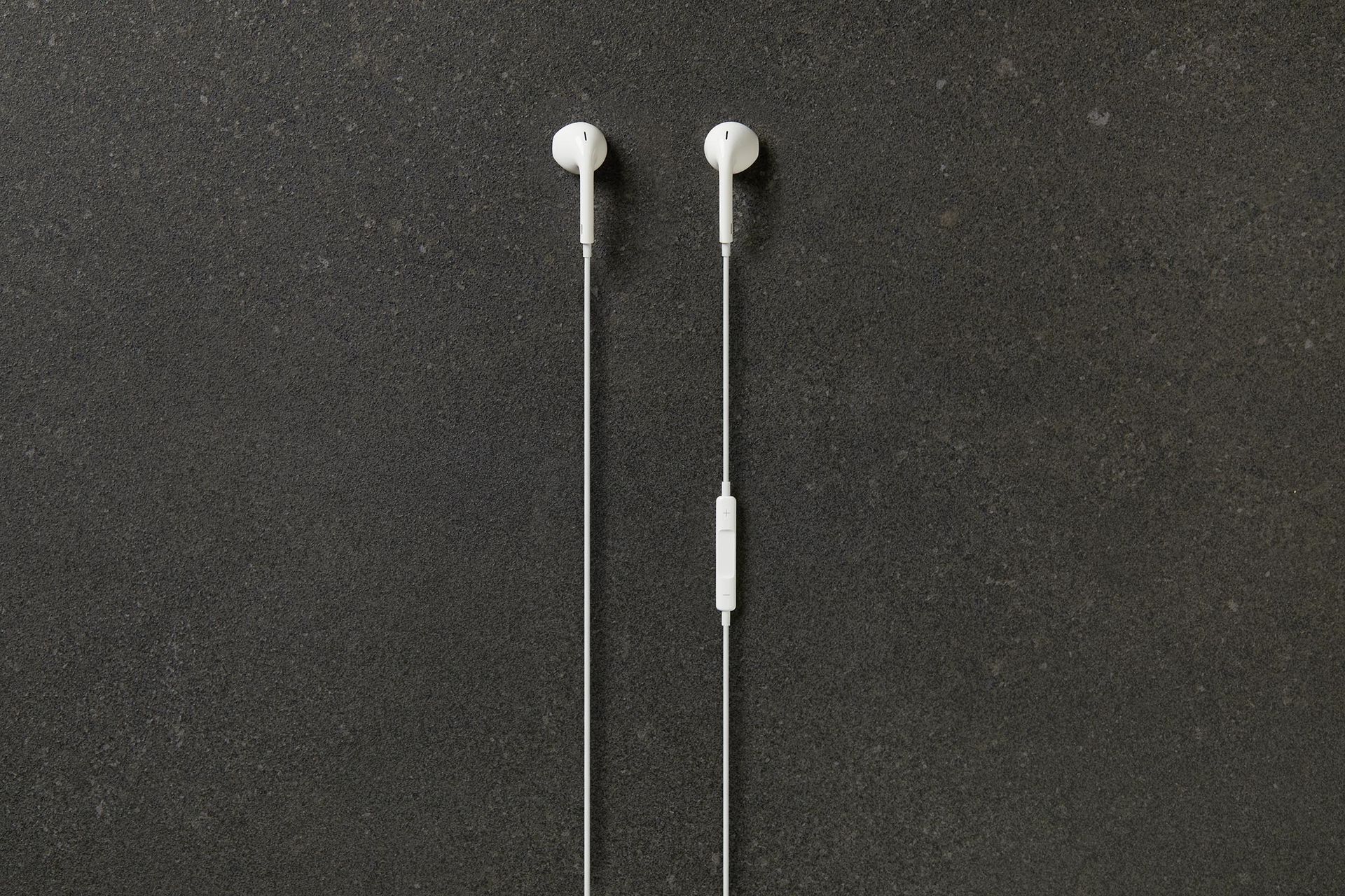 A pair of white ear buds sitting on top of a black surface.