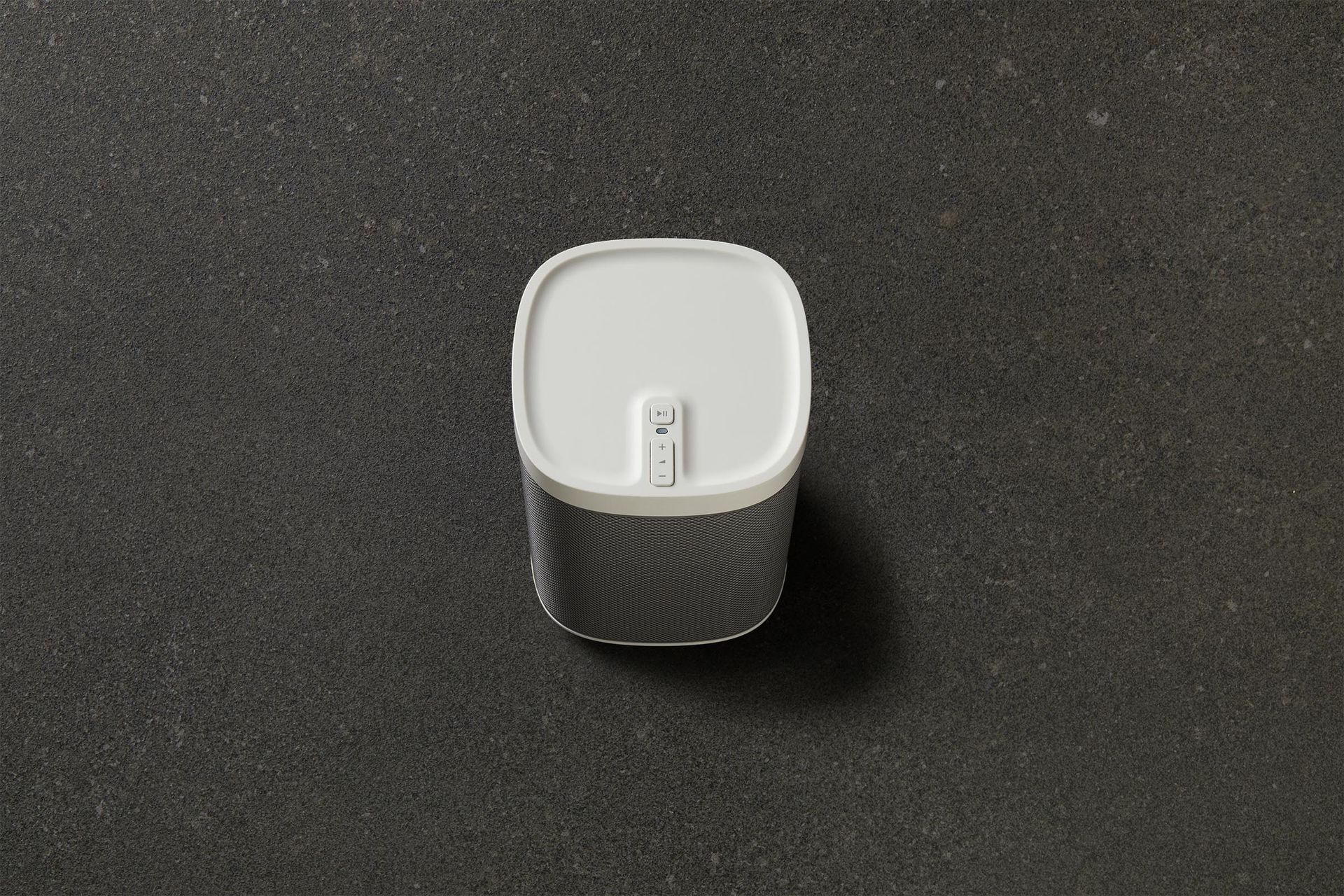 A white speaker is sitting on a black surface.