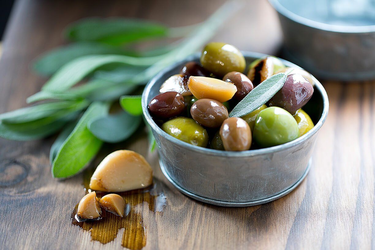 A bowl of olives and garlic on a wooden table.