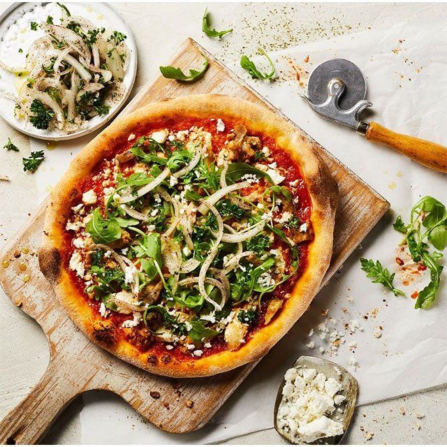 A pizza sitting on a wooden cutting board next to a pizza cutter