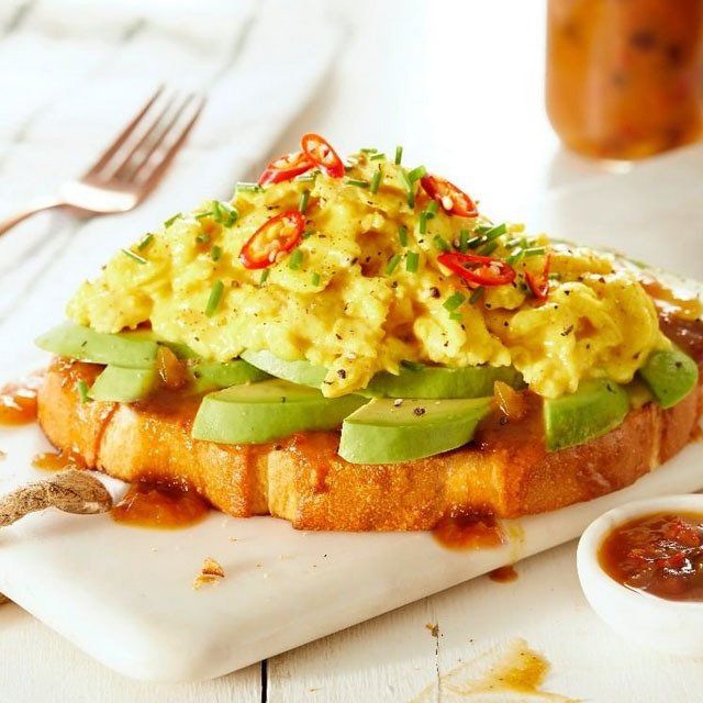 A sandwich with scrambled eggs and avocado on a cutting board