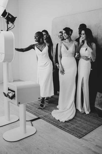 A group of women in white dresses are standing in front of a photo booth.