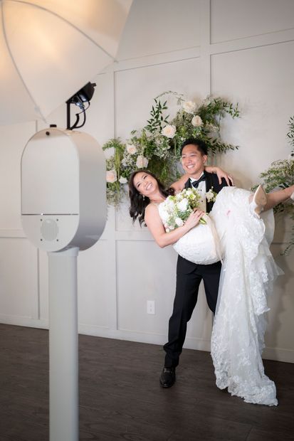 A man is holding a bride in his arms in front of a photo booth.