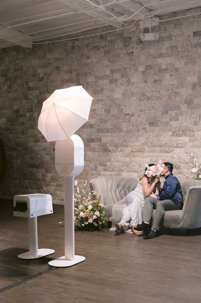 A bride and groom are kissing in front of a photo booth.