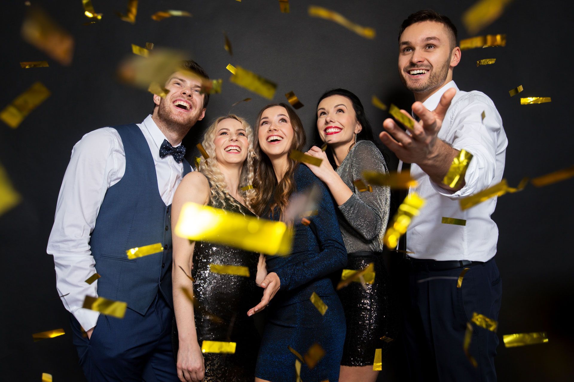 A group of people are standing in front of a wall with gold confetti falling from the sky.