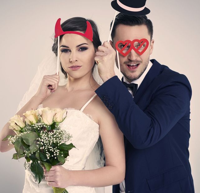 A bride and groom wearing devil horns and heart shaped glasses