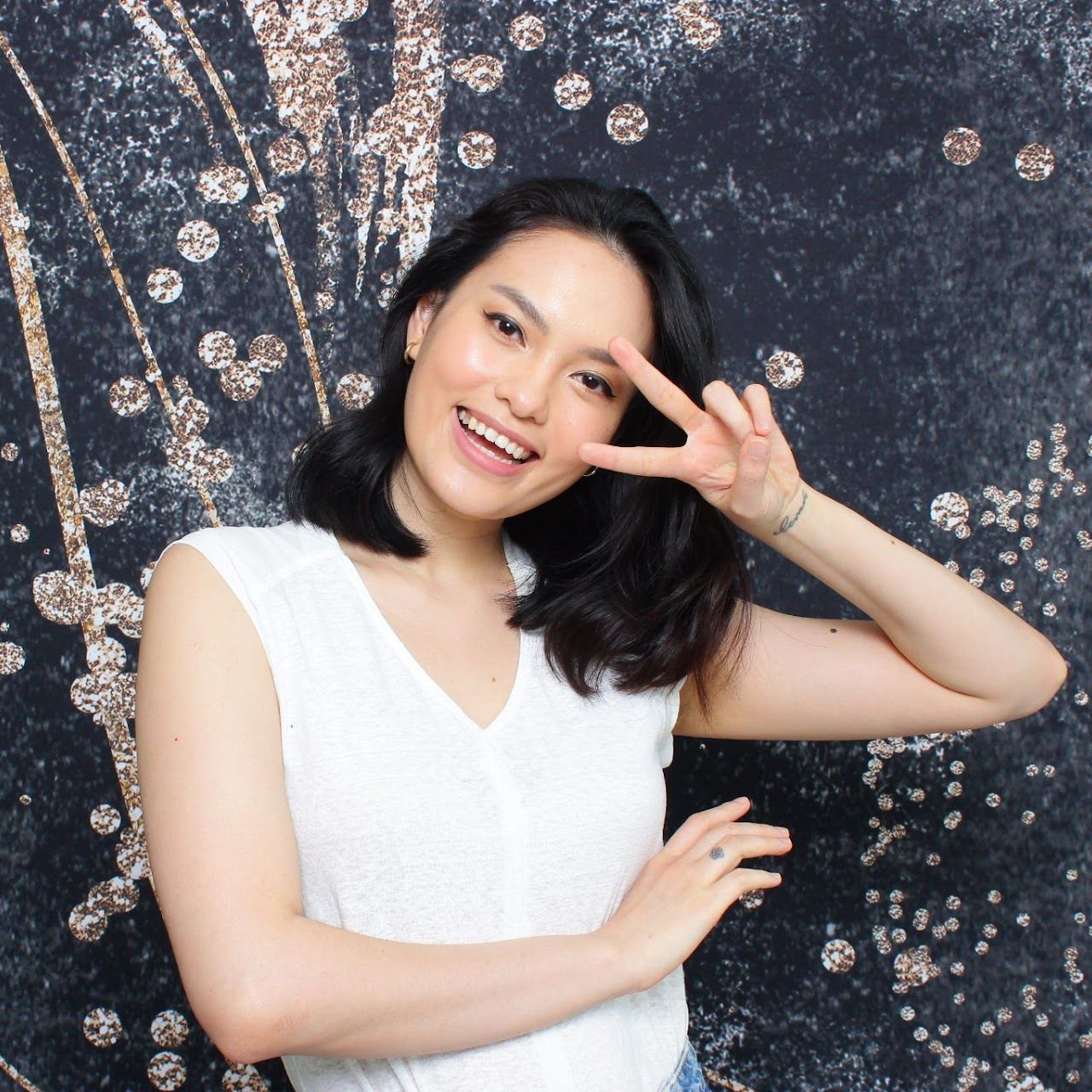 A woman in a white shirt is smiling and making a peace sign