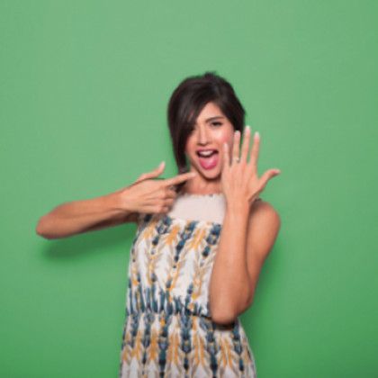 A woman in a dress is pointing at her hand in front of a green background.