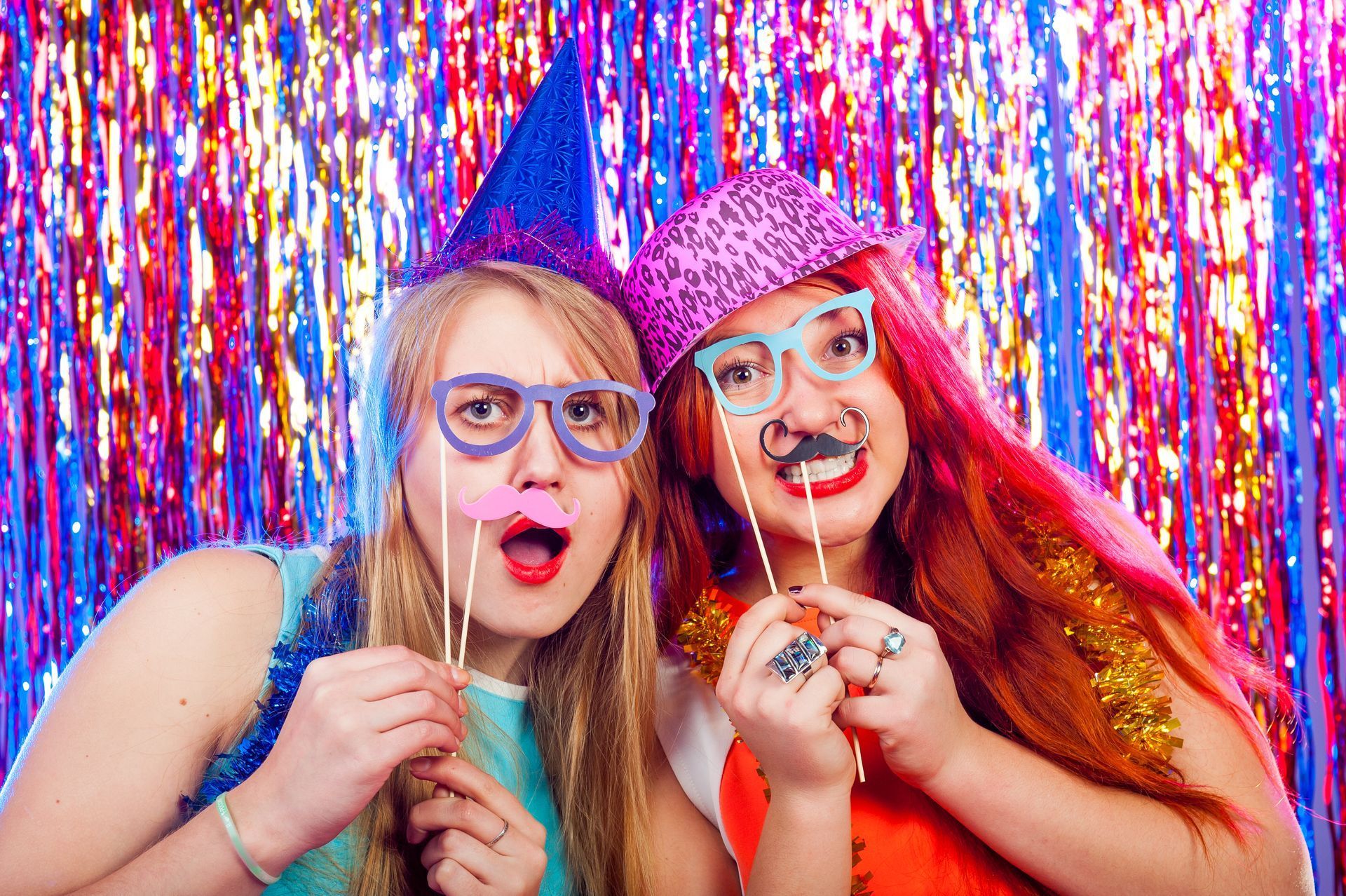 Two girls wearing party hats and fake mustaches are posing for a picture