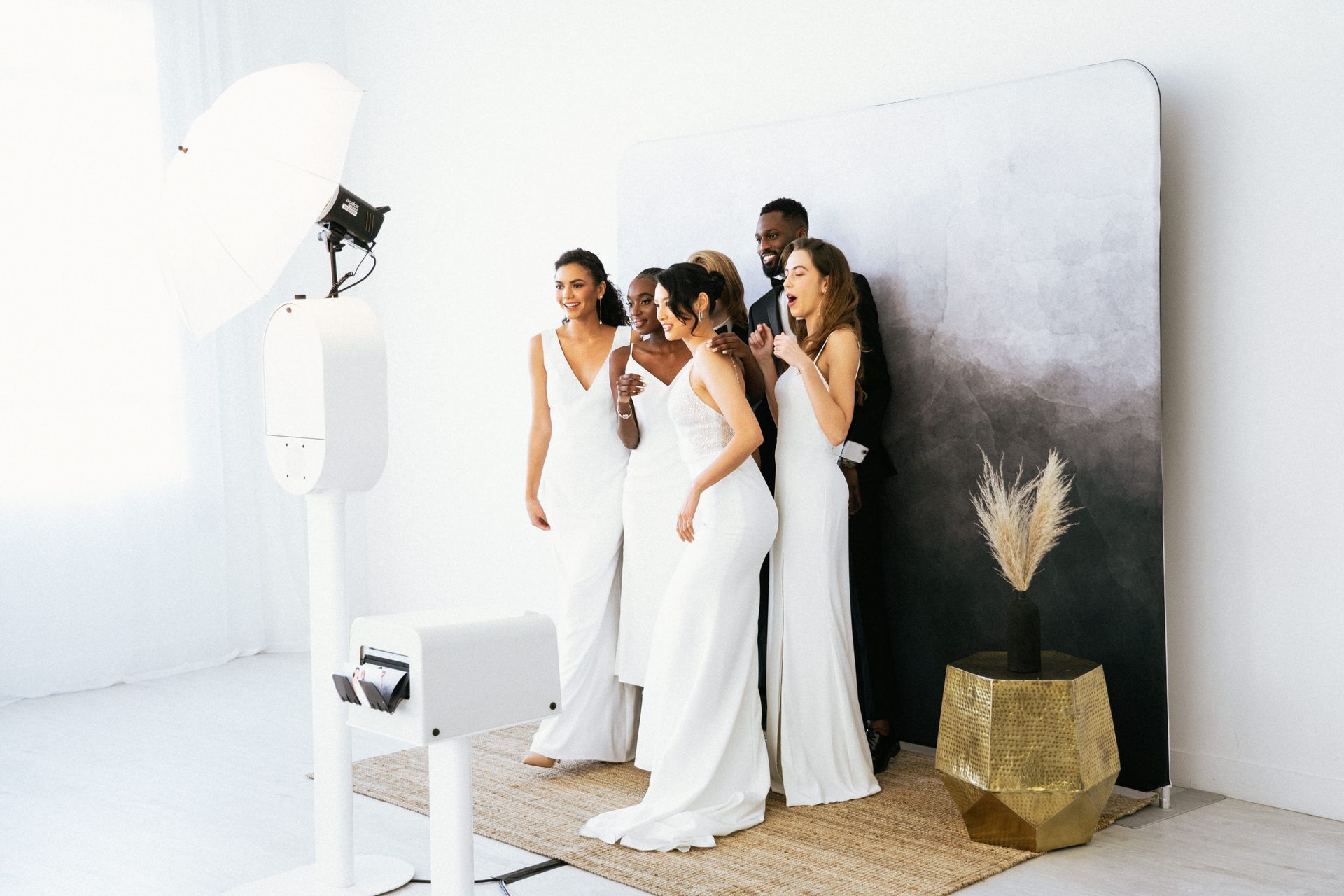 A group of women in white dresses are posing for a picture in front of a photo booth