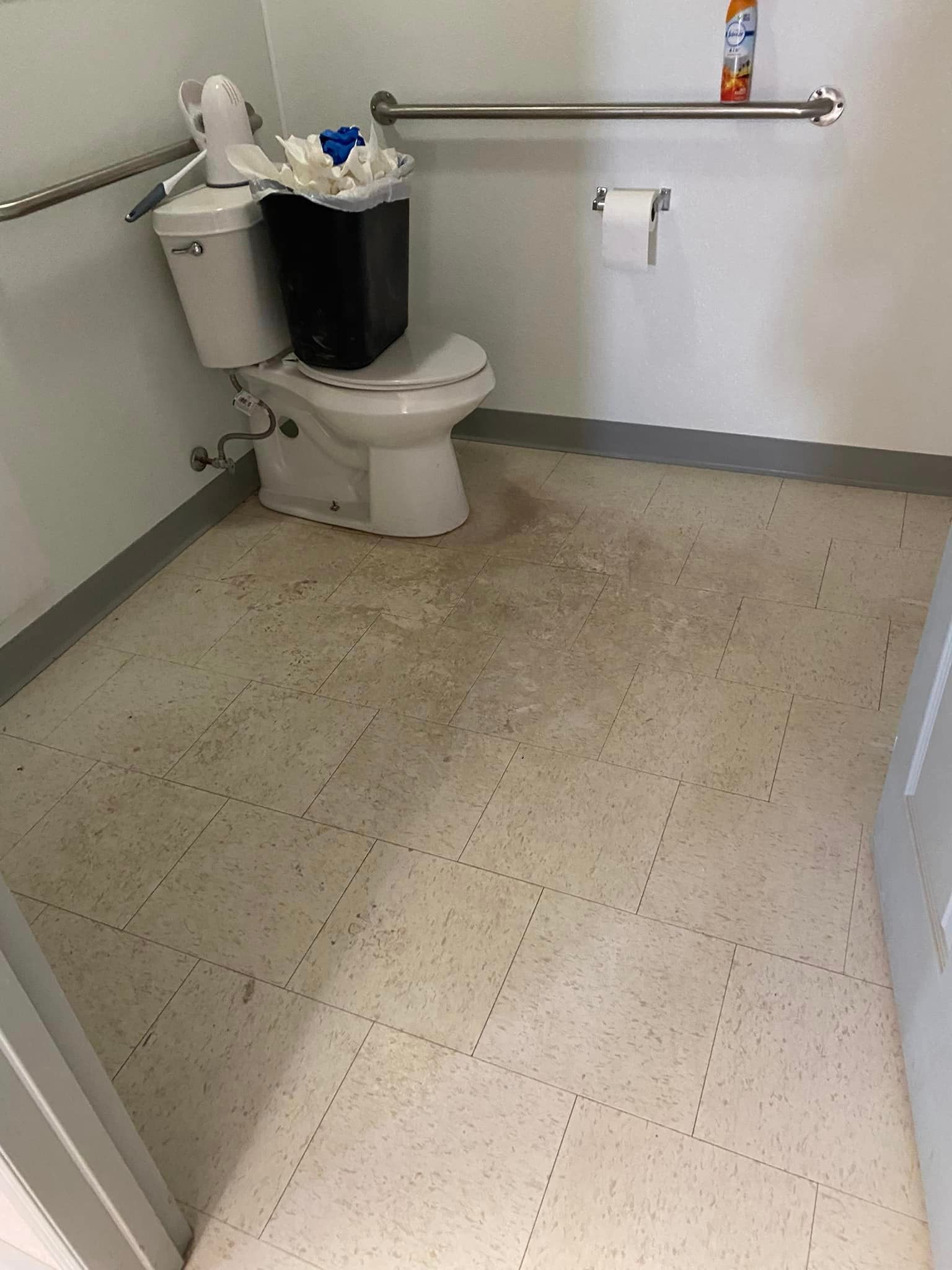 A bathroom with a toilet and a trash can on the floor.