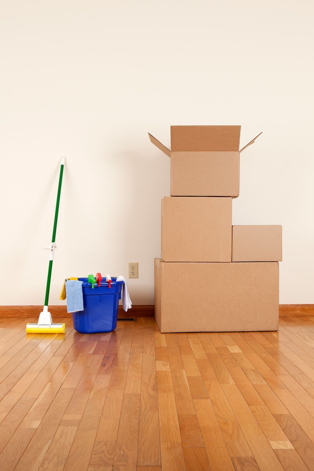 Empty room with wooden floor. Stack of cardboard boxes, cleaning supplies, and a mop near the wall.