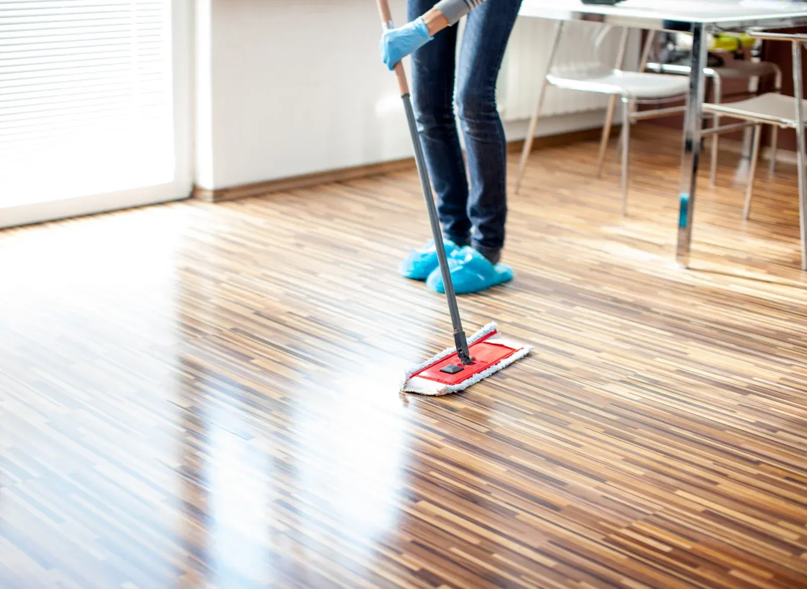 Person mopping a shiny wooden floor in a well-lit room.