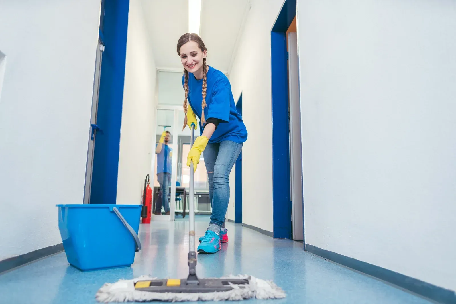 A woman is cleaning a hallway with a mop and bucket.