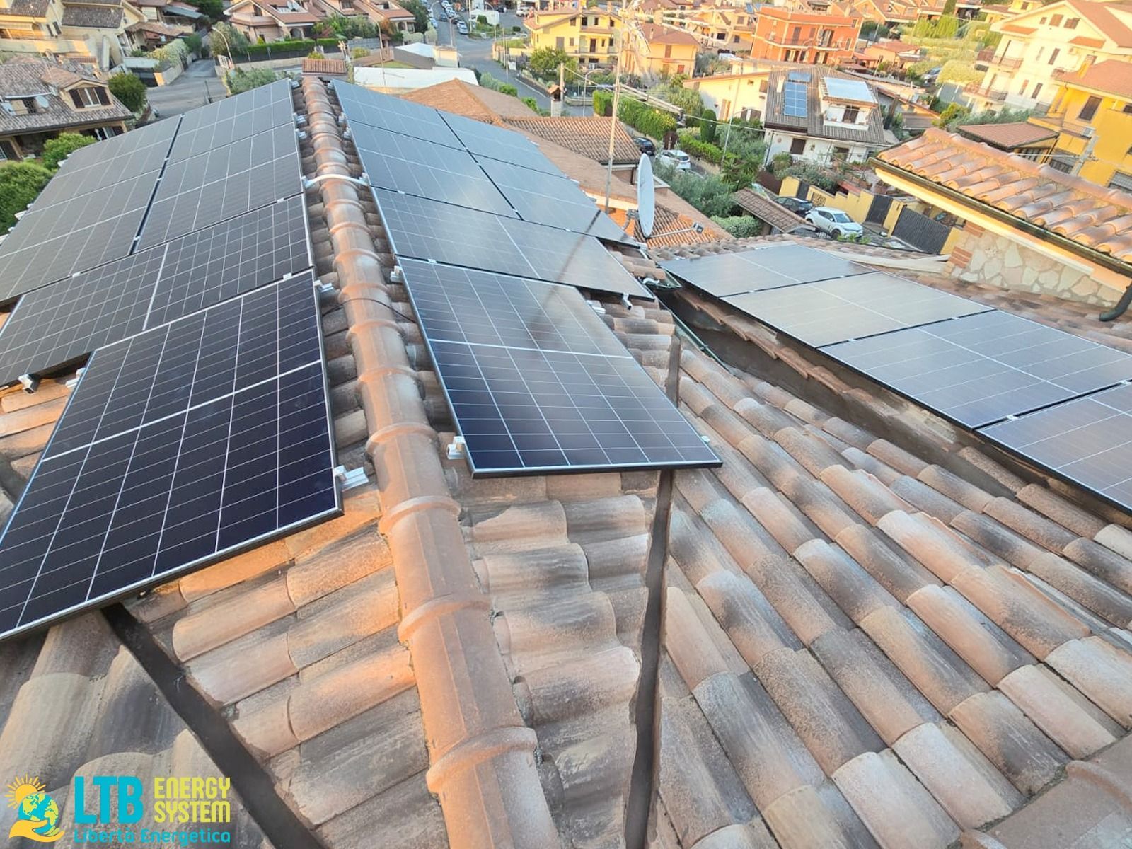 Pannelli solari installati su un tetto rivestito di tegole, con vista su una città europea. I pannelli sono neri, in contrasto con le tegole in terracotta.