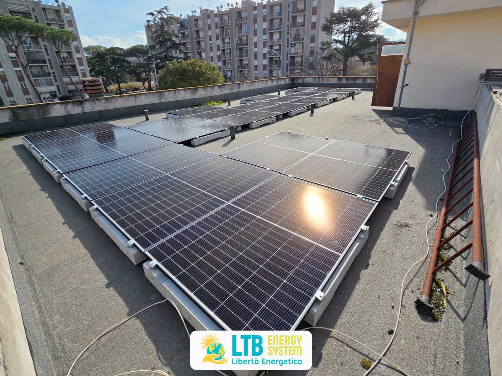 Pannelli solari installati su un tetto, disposti in modo rettangolare. I pannelli riflettono la luce solare e sono circondati da un muretto.