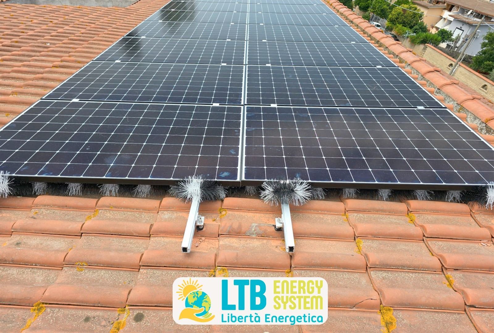 Pannelli solari installati su un tetto di tegole rosse. I pannelli sono neri con staffe di montaggio bianche; logo nell'angolo.