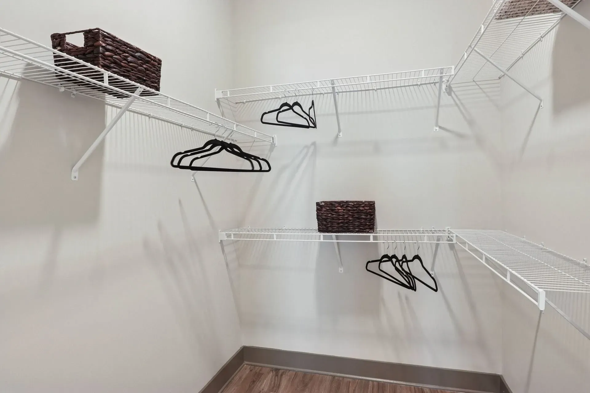 Walk-in closet with white wire shelves, hanging rods, and woven baskets.