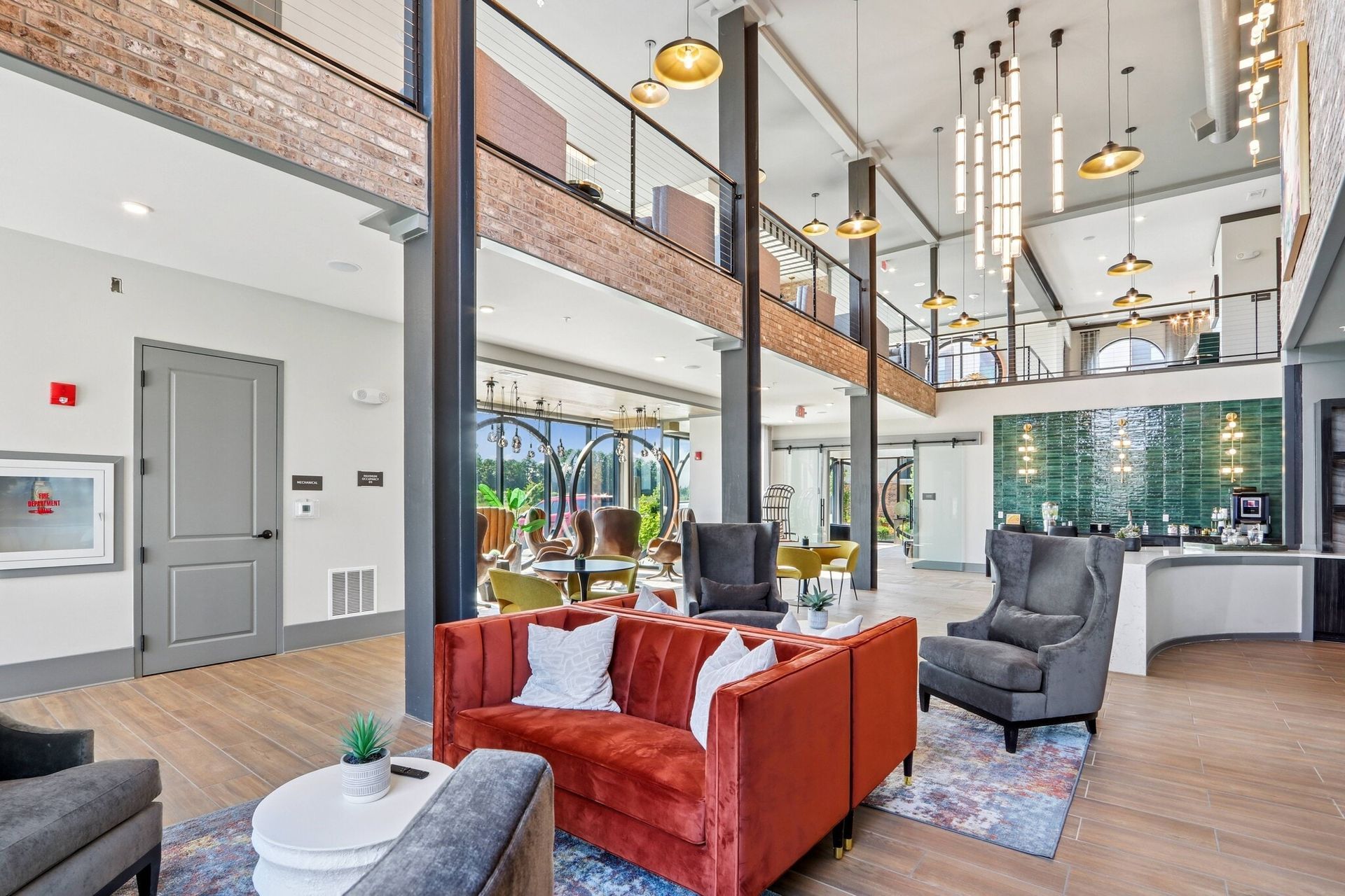 Spacious modern apartment lobby with orange sofa, gray lounge chairs, and a mezzanine.