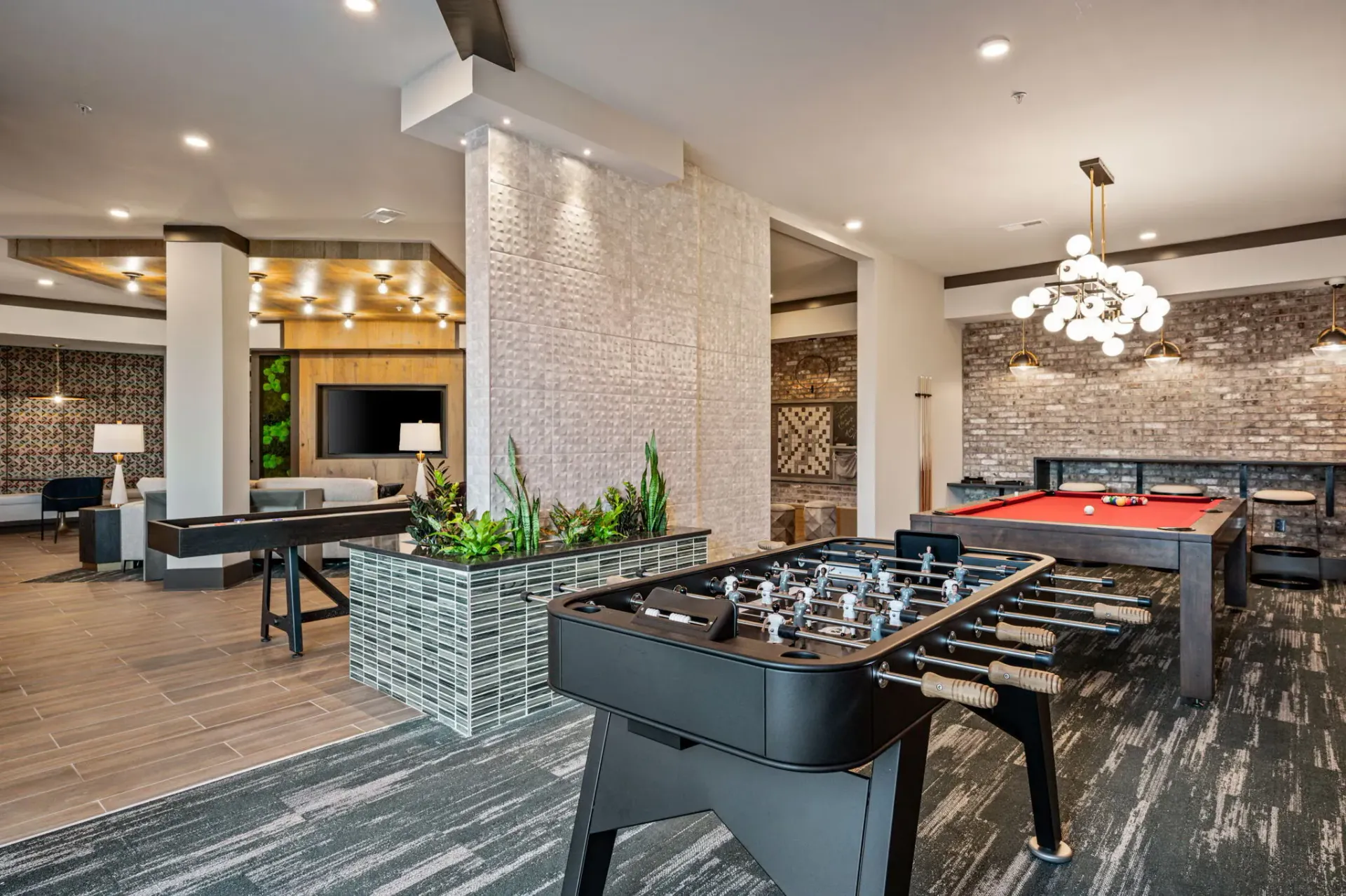 Modern indoor community lounge with foosball and pool tables, seating and stylish lighting.