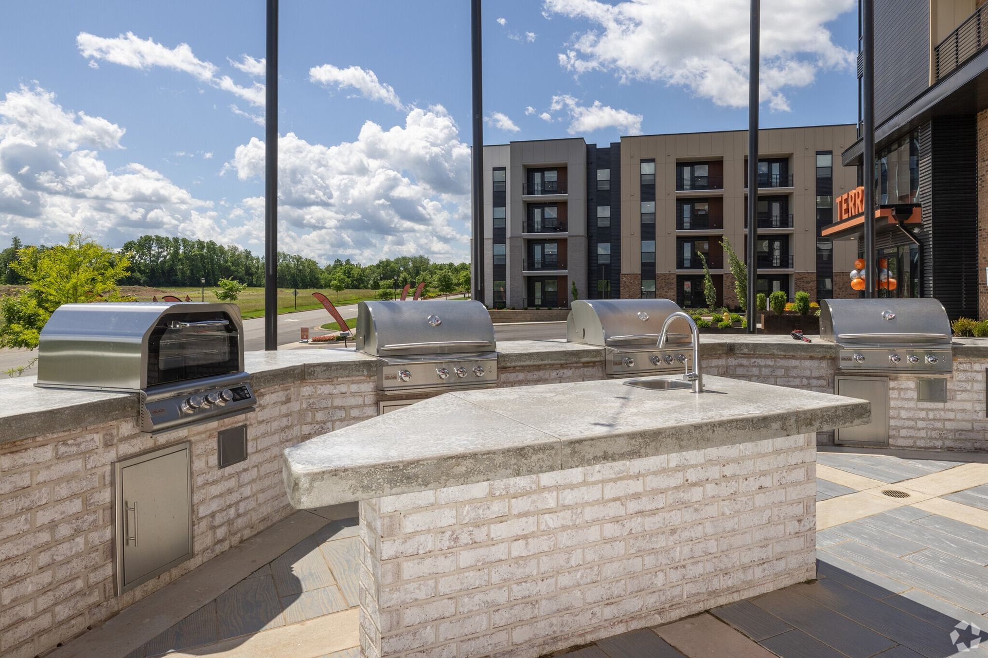 Outdoor community grill area with stainless steel grills and brick counters.