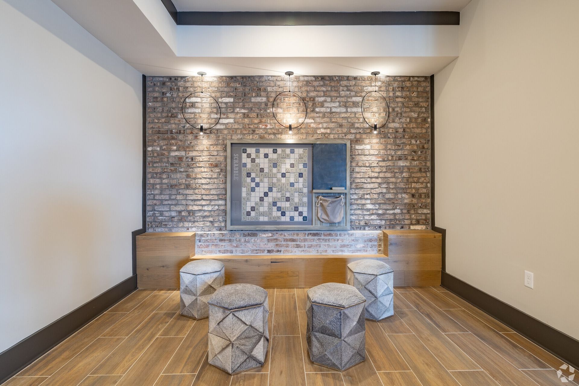 Indoor community lounge with brick wall, circular pendant lights, and wooden seating.