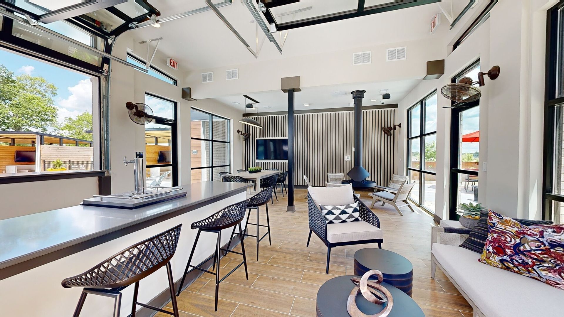 Modern community lounge with bar seating, large windows, and a central fireplace.