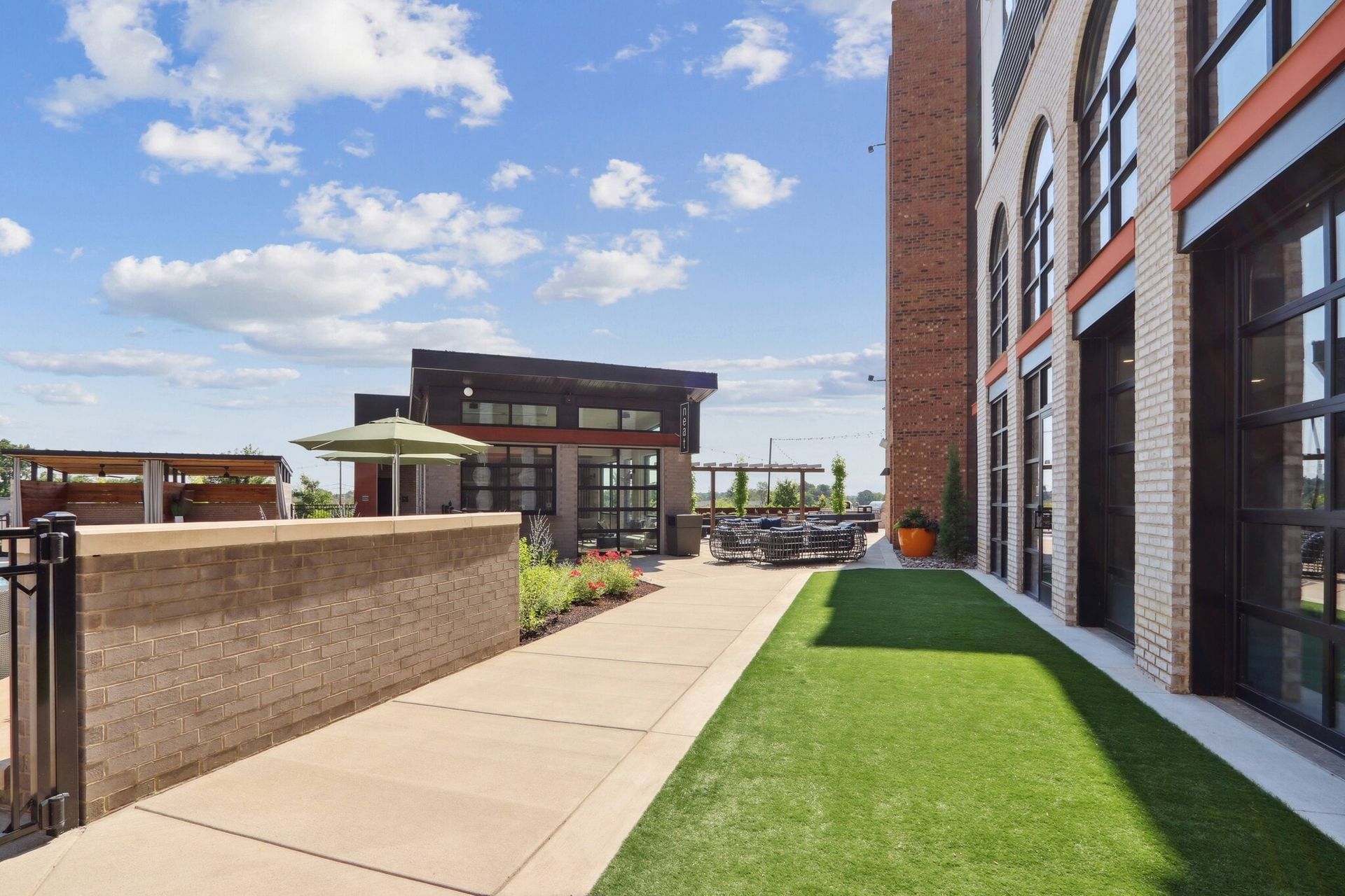 Outdoor rooftop terrace with seating, umbrellas, and greenery by a brick building.