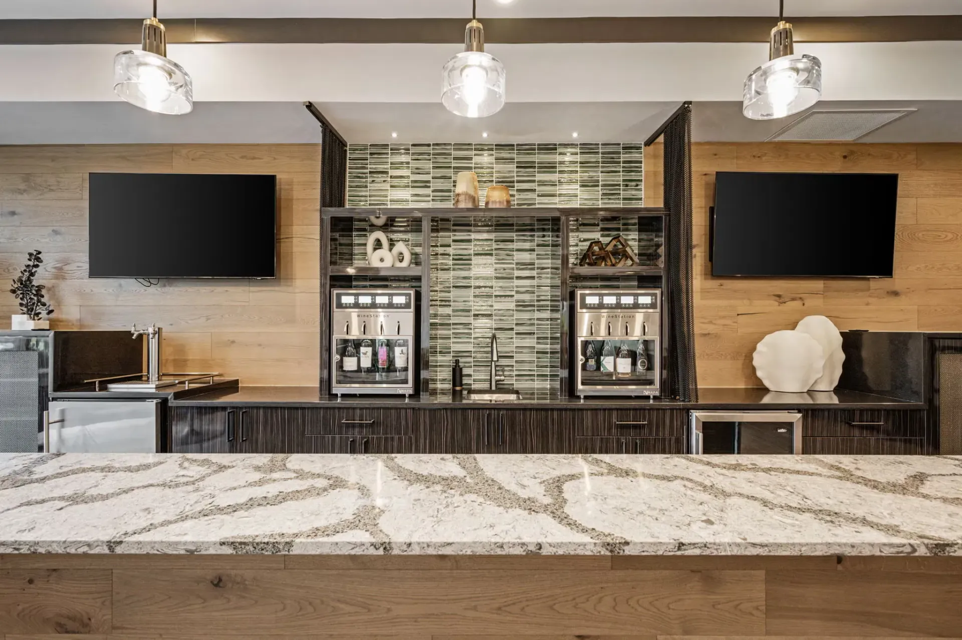 Amenity kitchen area with two beverage machines, glass tile backsplash, and a granite island.