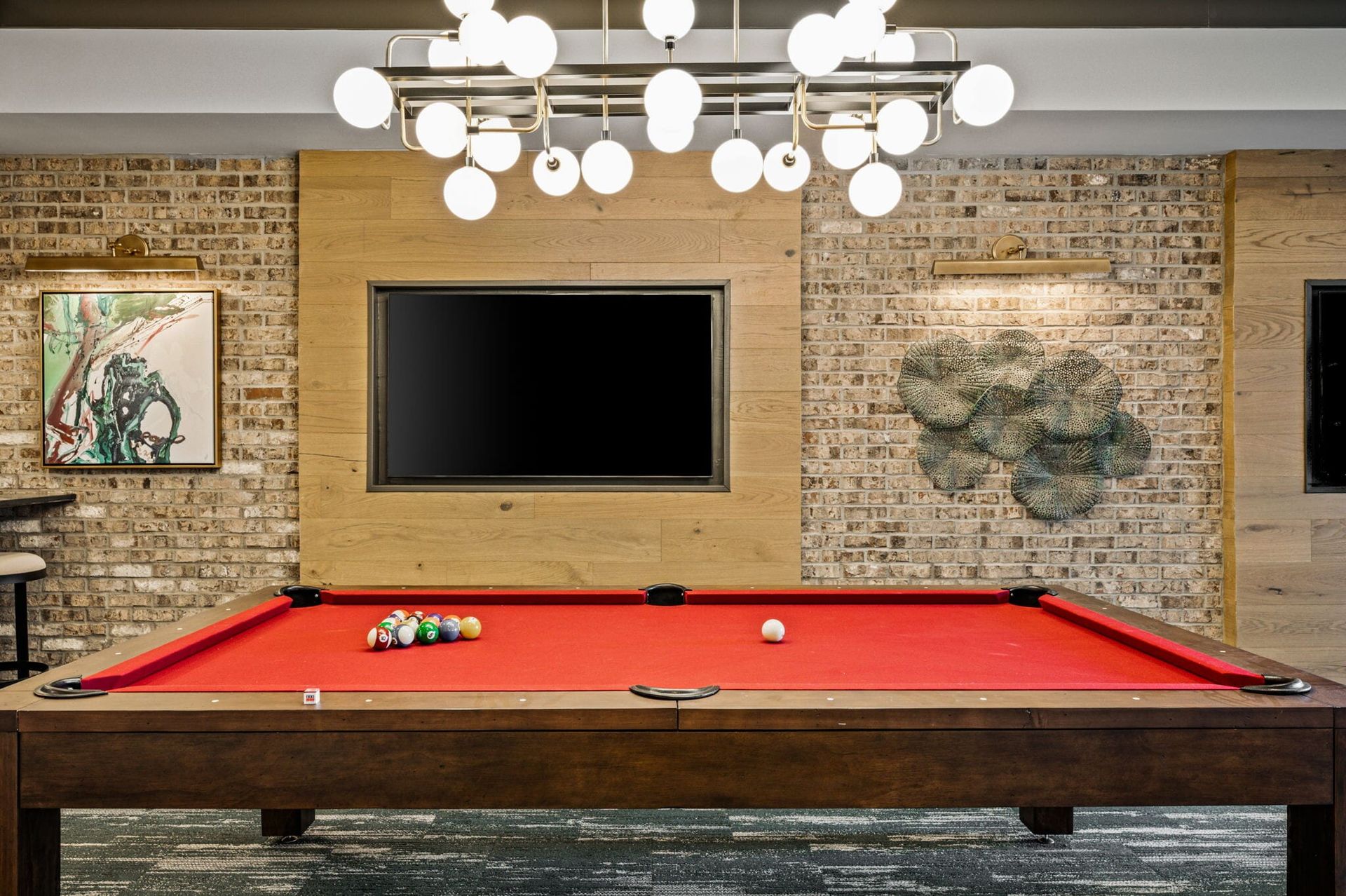 Indoor community recreation room with a red pool table, brick walls, and modern pendant lighting.