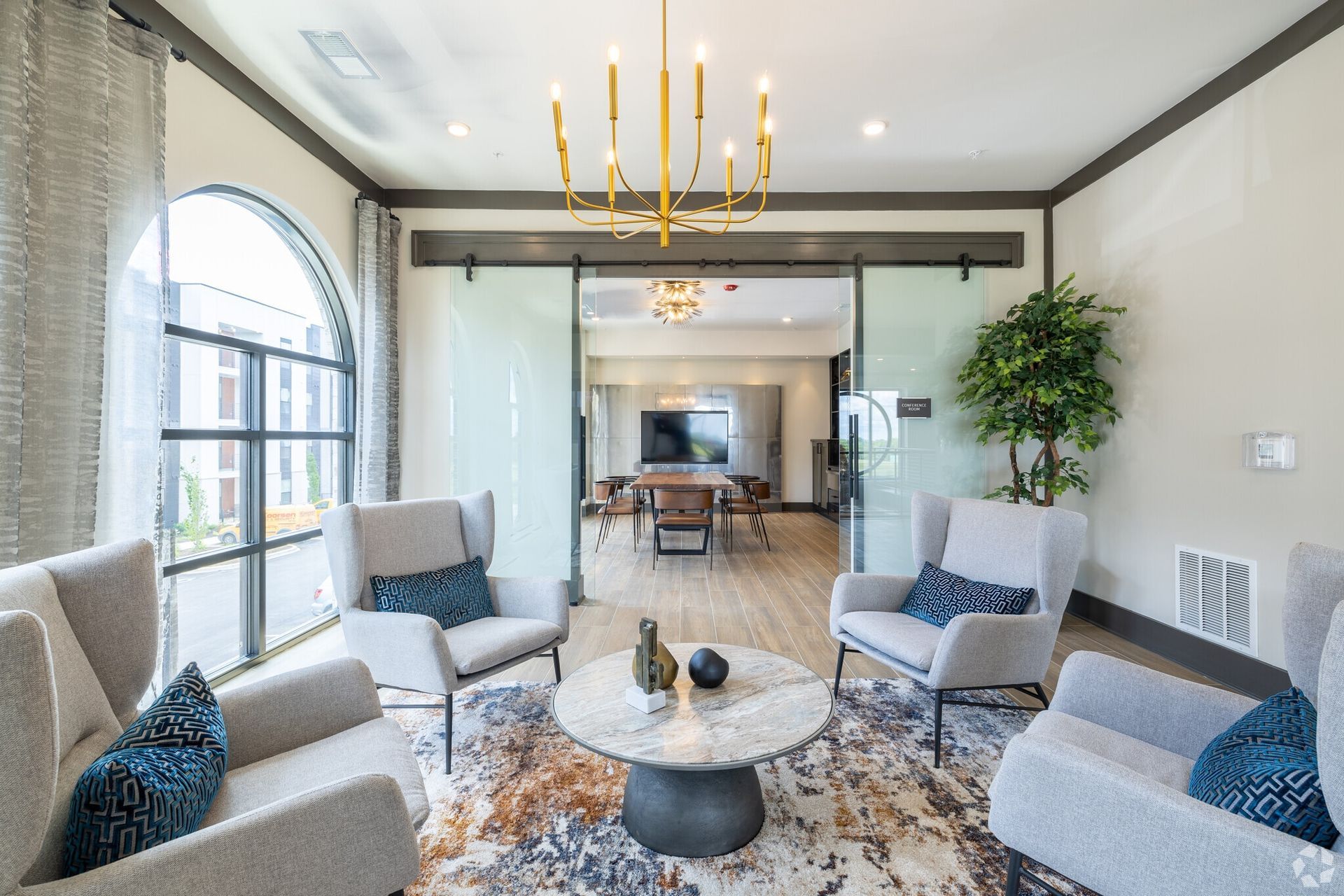 Modern resident lounge with four beige armchairs around a round marble table and glass sliding doors.
