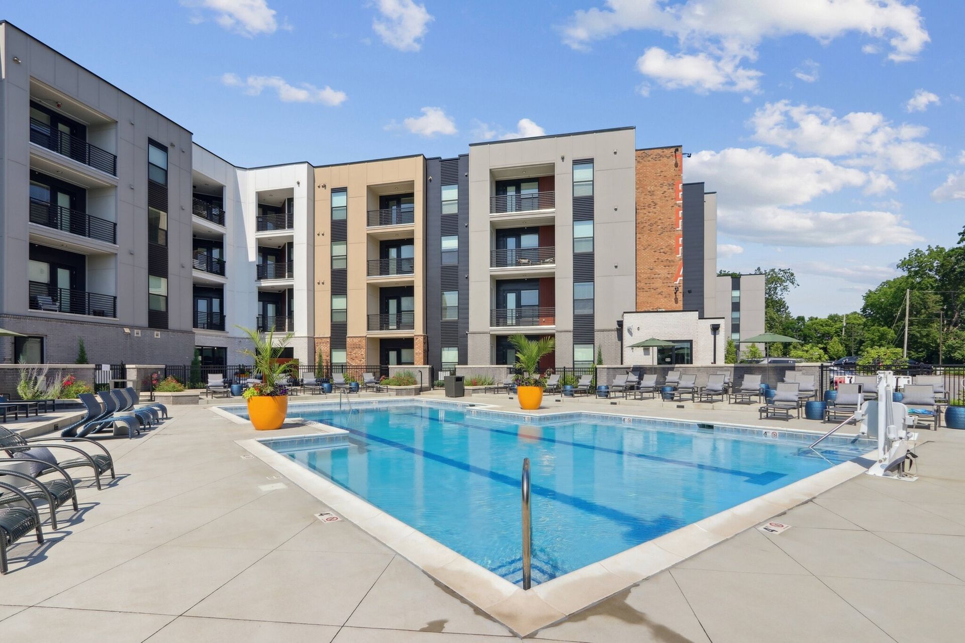 Outdoor swimming pool area at a modern apartment complex with lounge chairs.