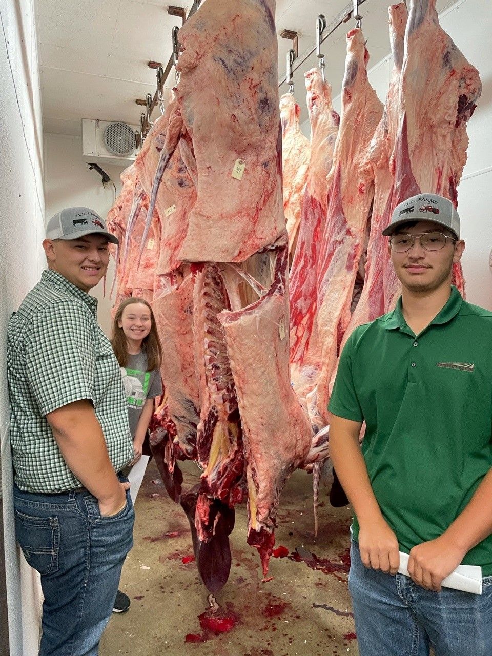 Two men are standing in front of a large piece of meat hanging from the ceiling.