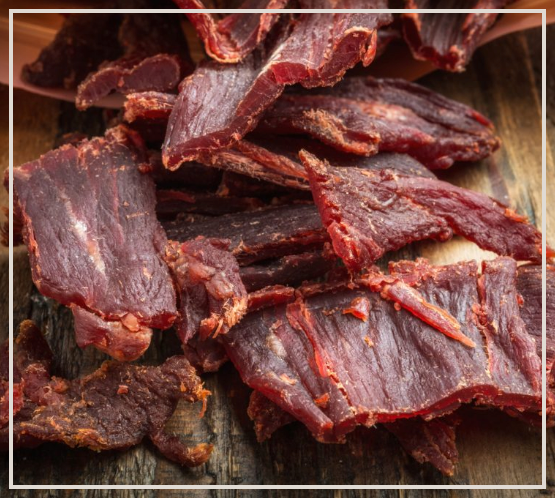 A pile of beef jerky is sitting on a wooden table.