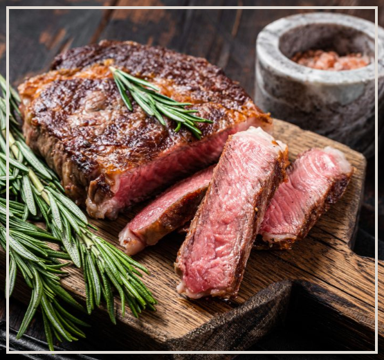 A steak is sitting on a wooden cutting board with rosemary.