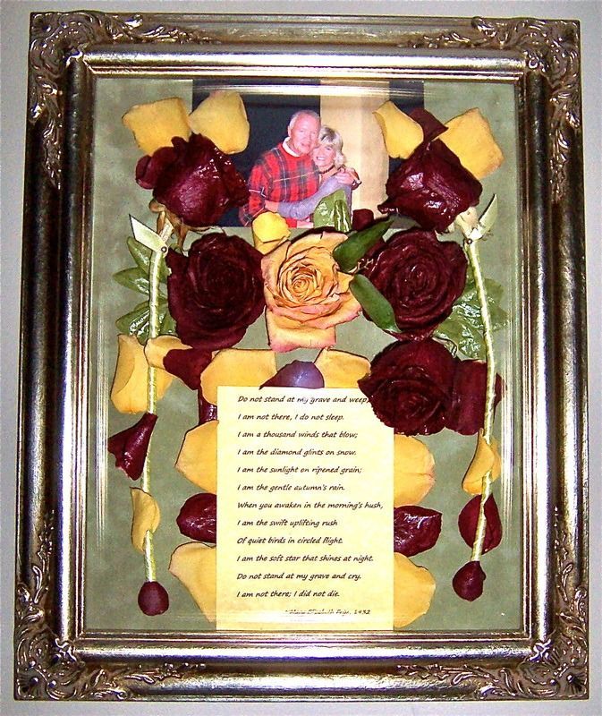 Framed floral arrangement with red roses, yellow petals, and a small centered message card