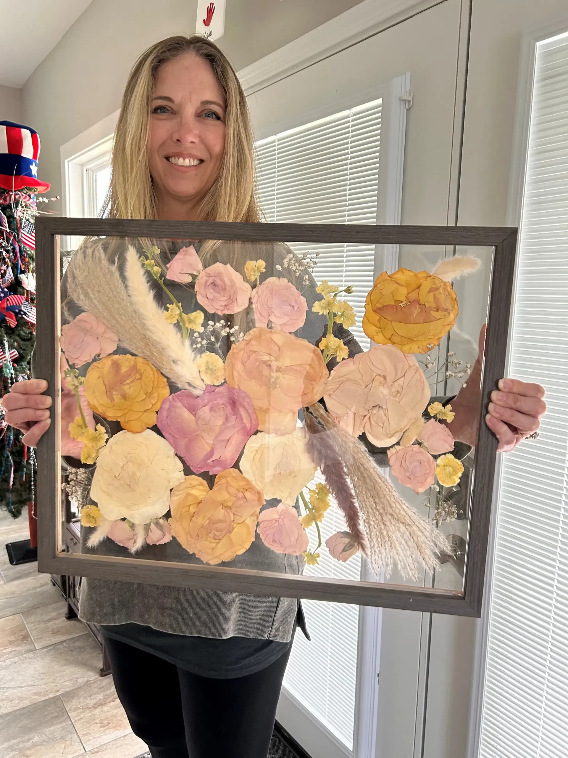Woman holding a framed floral collage artwork indoors.