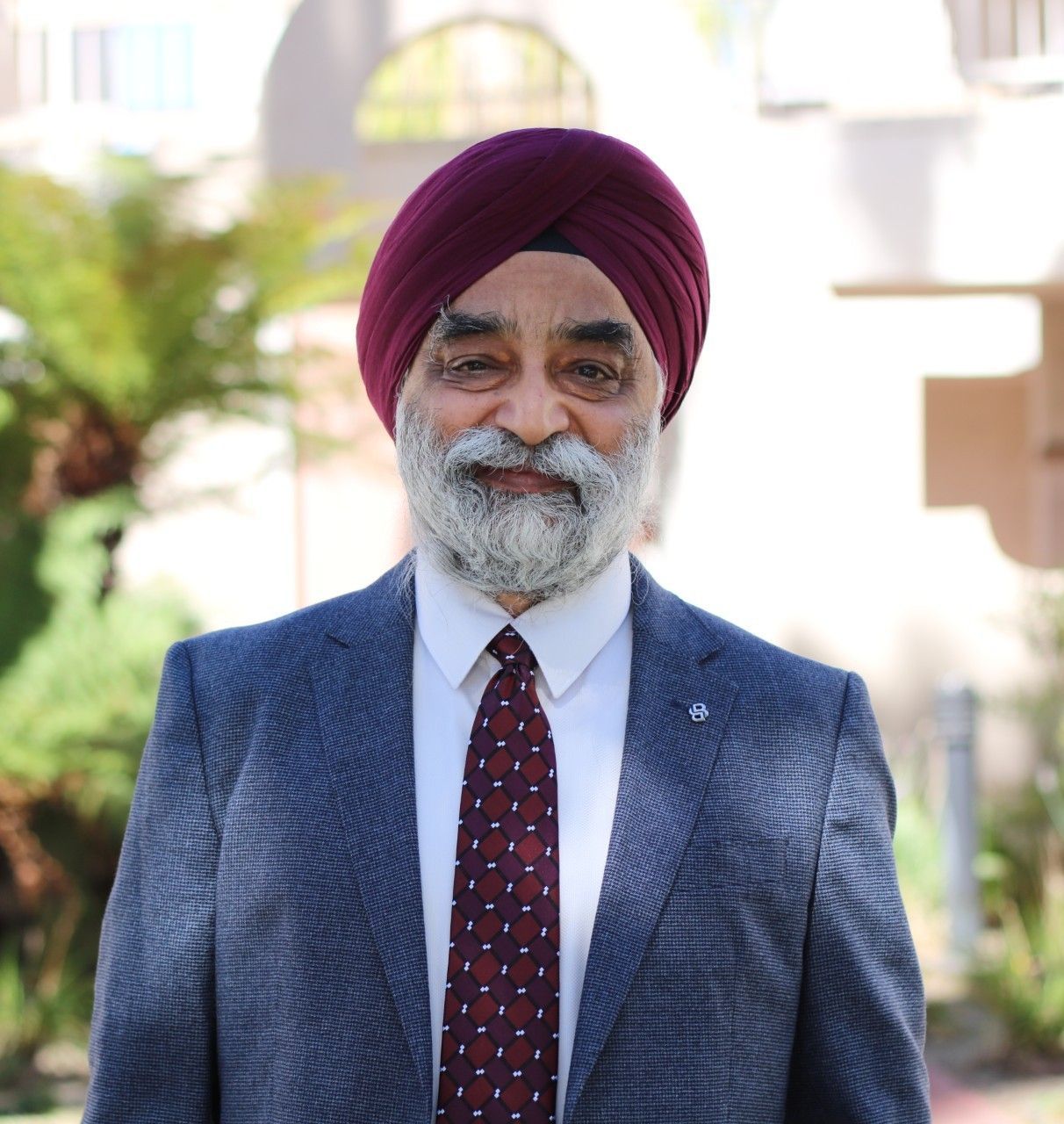 A smiling older man with a maroon turban and beard