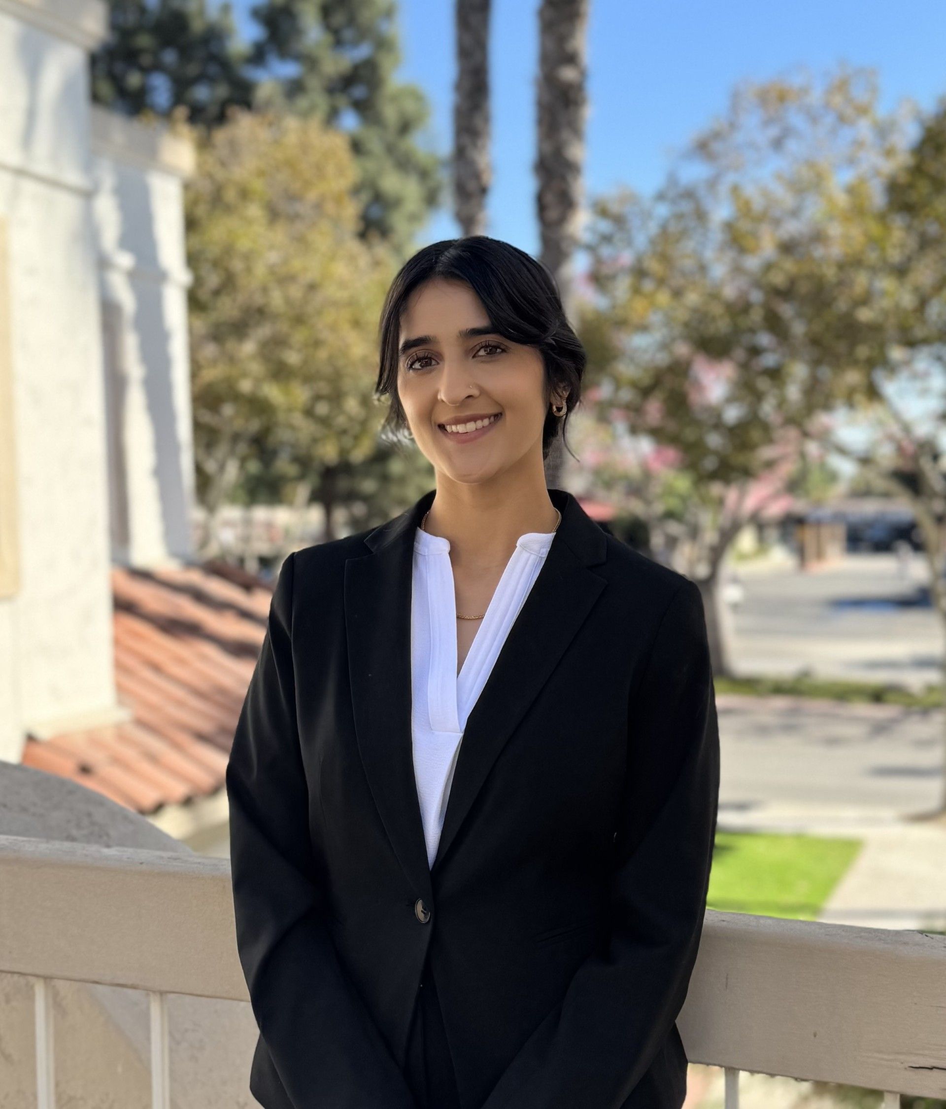 Woman with dark hair wearing a black blazer and white shirt smiles outdoors.