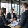 Three professionals in business attire sit around a wooden table in an office, reviewing documents during a meeting.