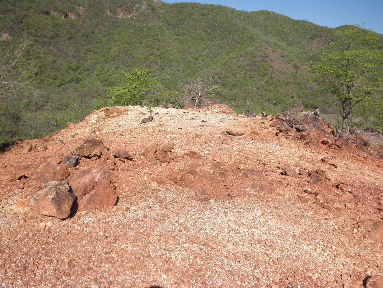 A pile of dirt and rocks on top of a hill with mountains in the background