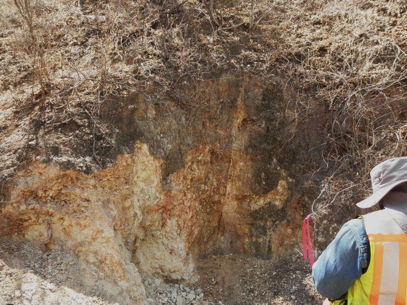 A man wearing a hat and safety vest is standing in front of a large rock.