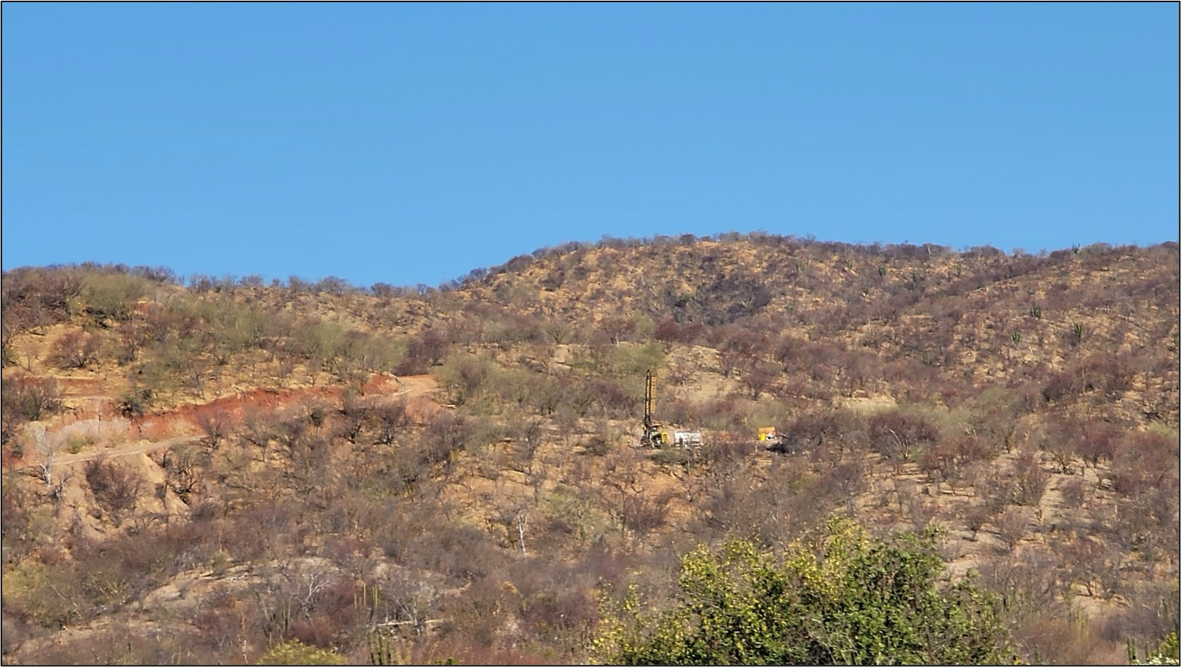 Photo 1. Core drill rig setting up on the south end of the Main Zone Trend targeting the depth projection of the red oxidized material exposed along a road cut left of center on the image.