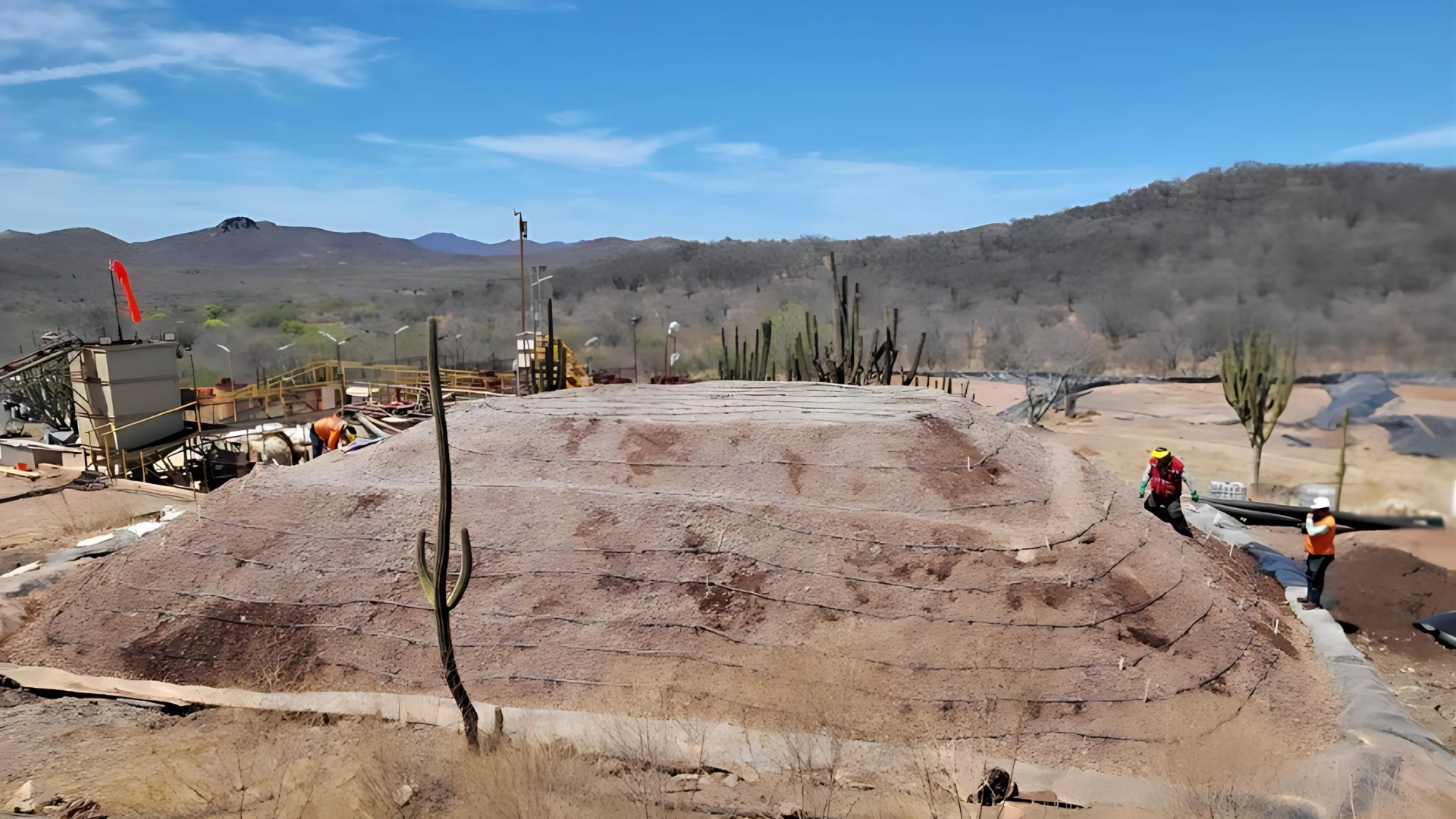 A large pile of dirt in the middle of a desert with mountains in the background.