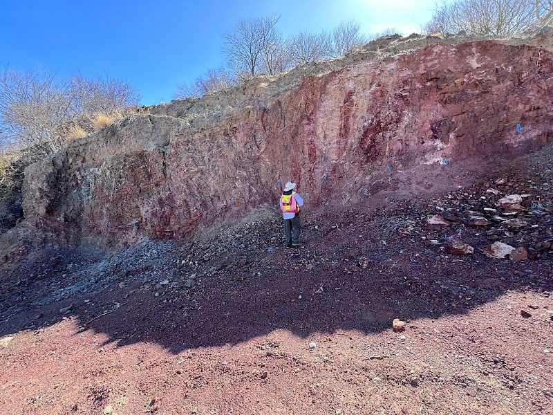 A man in a hard hat is standing on top of a rocky hill.