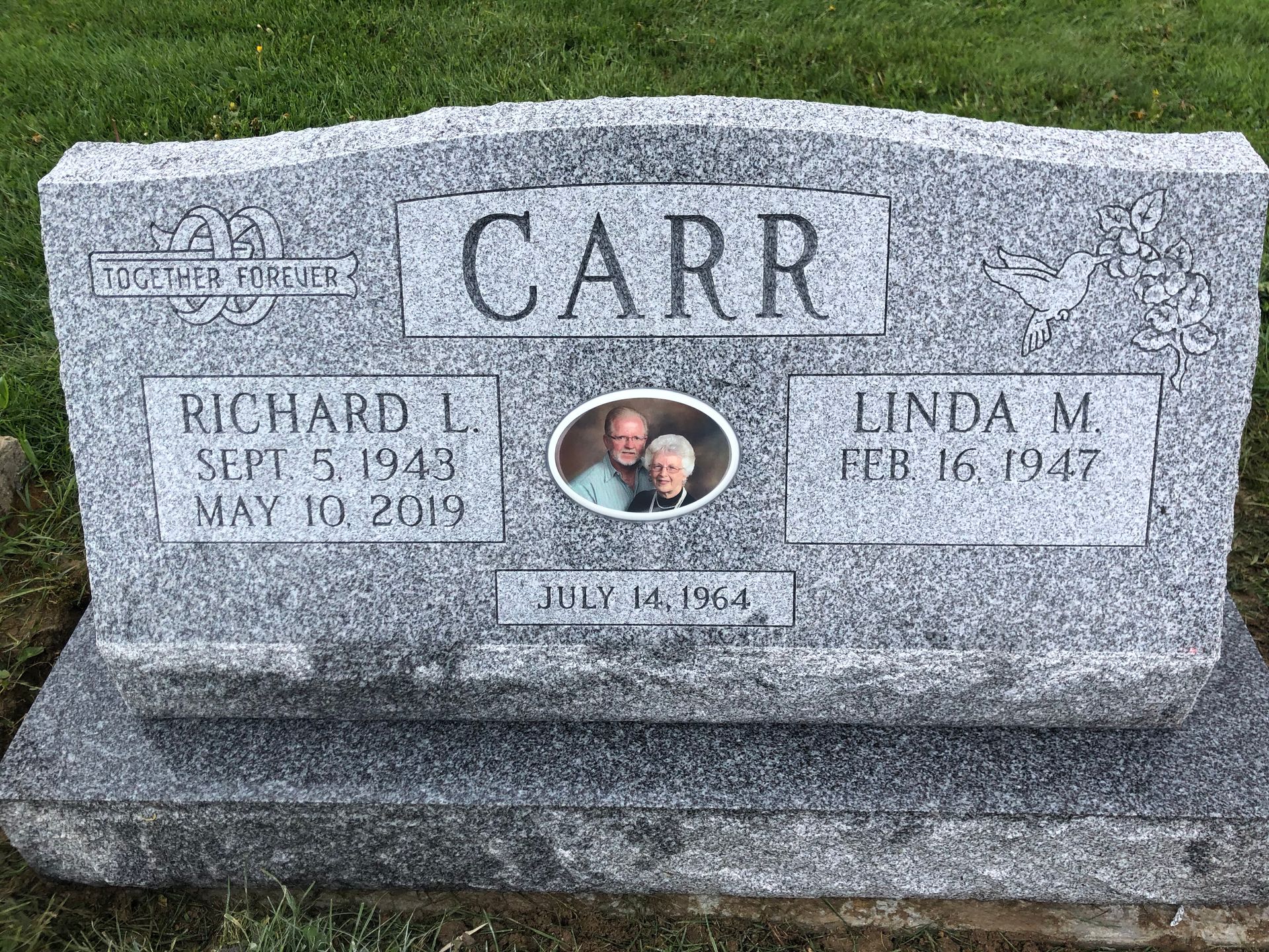 Cemetery with numerous headstones on a grassy lawn; trees casting shadows.