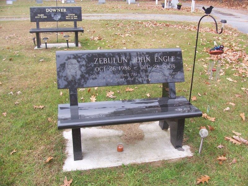 Granite bench in a cemetery, other headstones and flowers visible in the background.