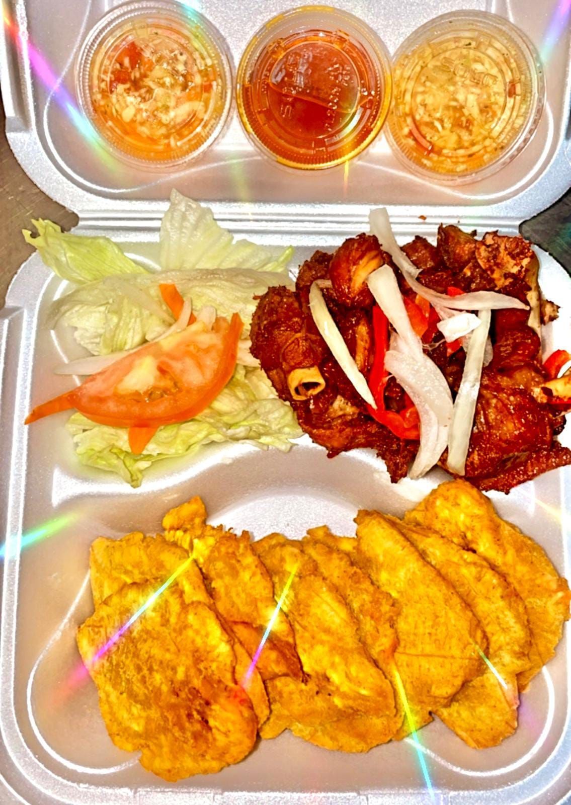 A styrofoam container filled with fried food and sauces.