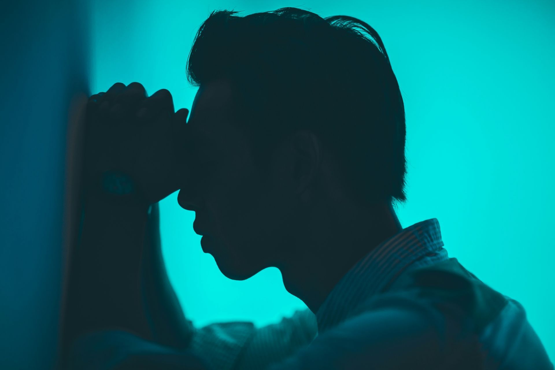 A silhouette of a man holding his head against a wall.